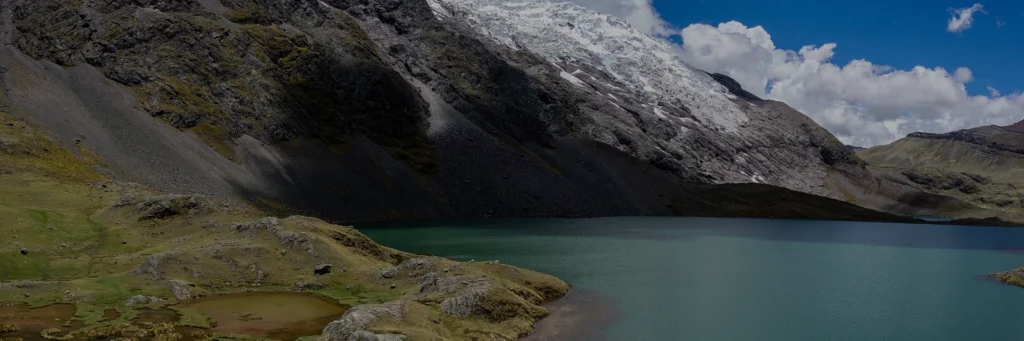 Serene sunset reflecting on a lake surrounded by dense forests and snow-capped mountains in Ausangate, Cusco, Peru, Kaymara Luxury Travel.
