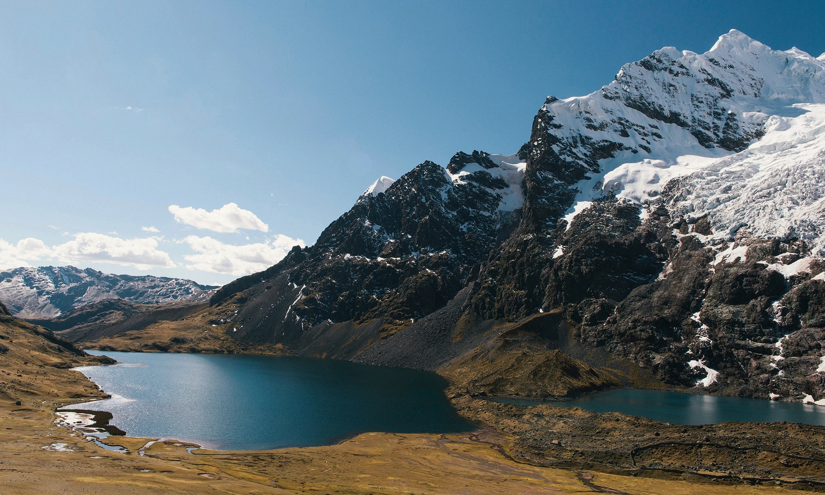 Tranquil lake reflecting a clear blue sky and snow-capped mountains in the Ausangate region, Cusco, Peru, Kaymara Luxury Travel.