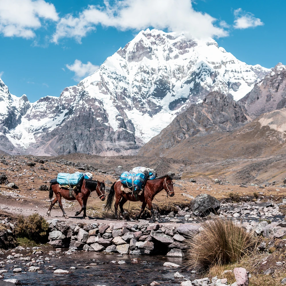 Serene river flowing through a lush green valley with snow-capped mountains in the Ausangate region, Cusco, Peru, Kaymara Luxury Travel.